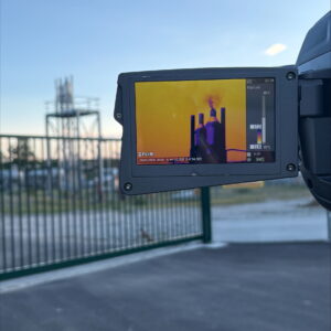En arrière plan, une infrastructure gazière, en premier plan l'écran d'une caméra infrarouge qui filme cette infrastructure et qui révèle du gaz qui s'en échappe